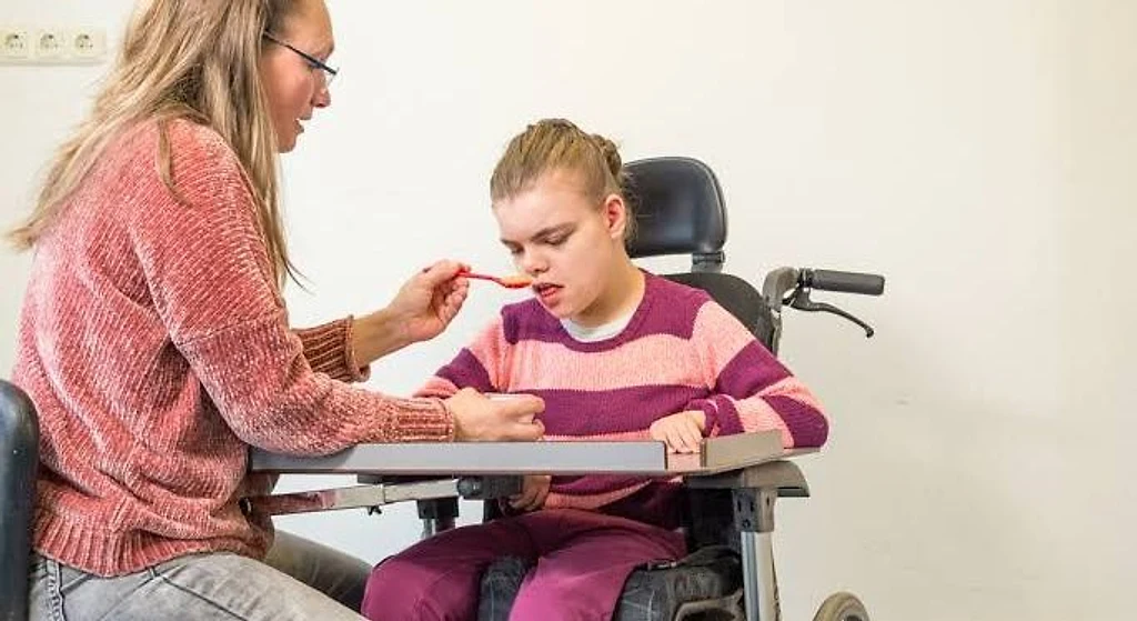 A support worker assisting a young participant with her meal