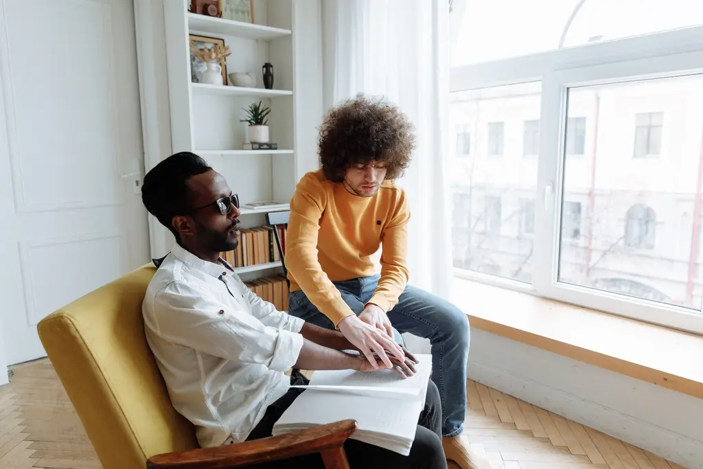 A support worker helping a man read braille at home