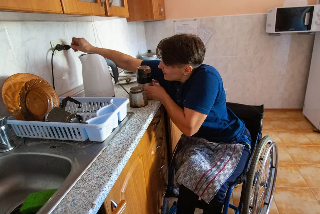 A young man in a wheelchair washing up at his kitchen sink