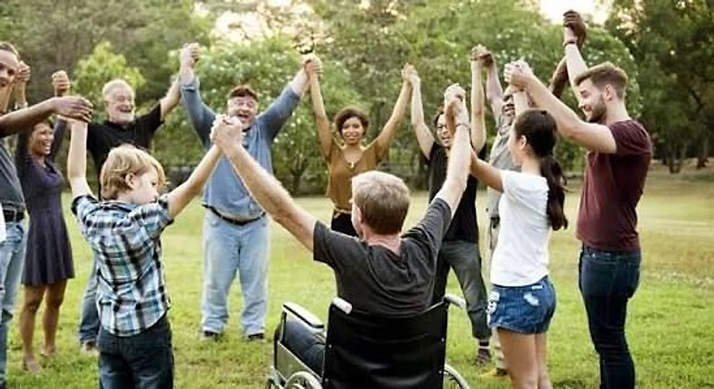 A wide circle of people holding hands together in a park