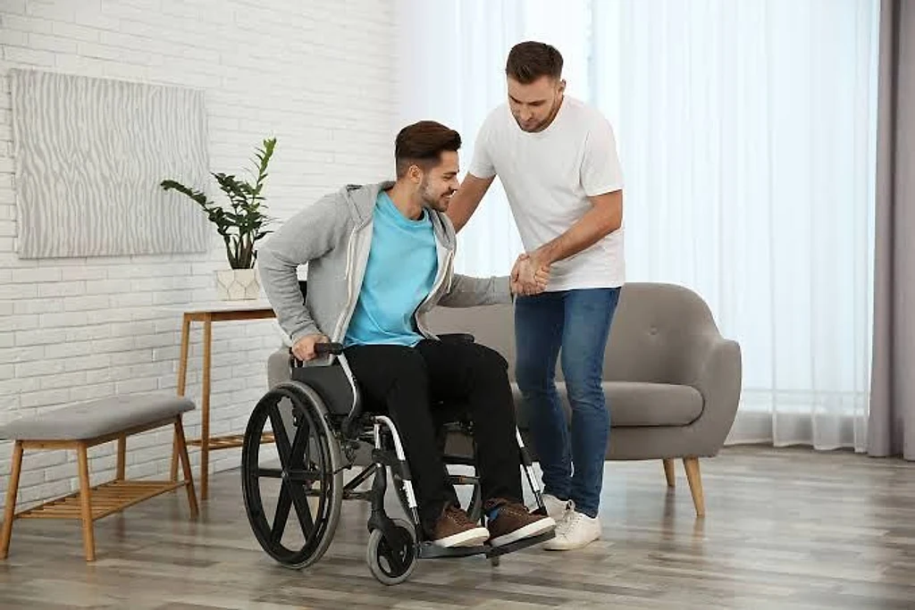 A support worker helping a young man stand from his wheelchair at home