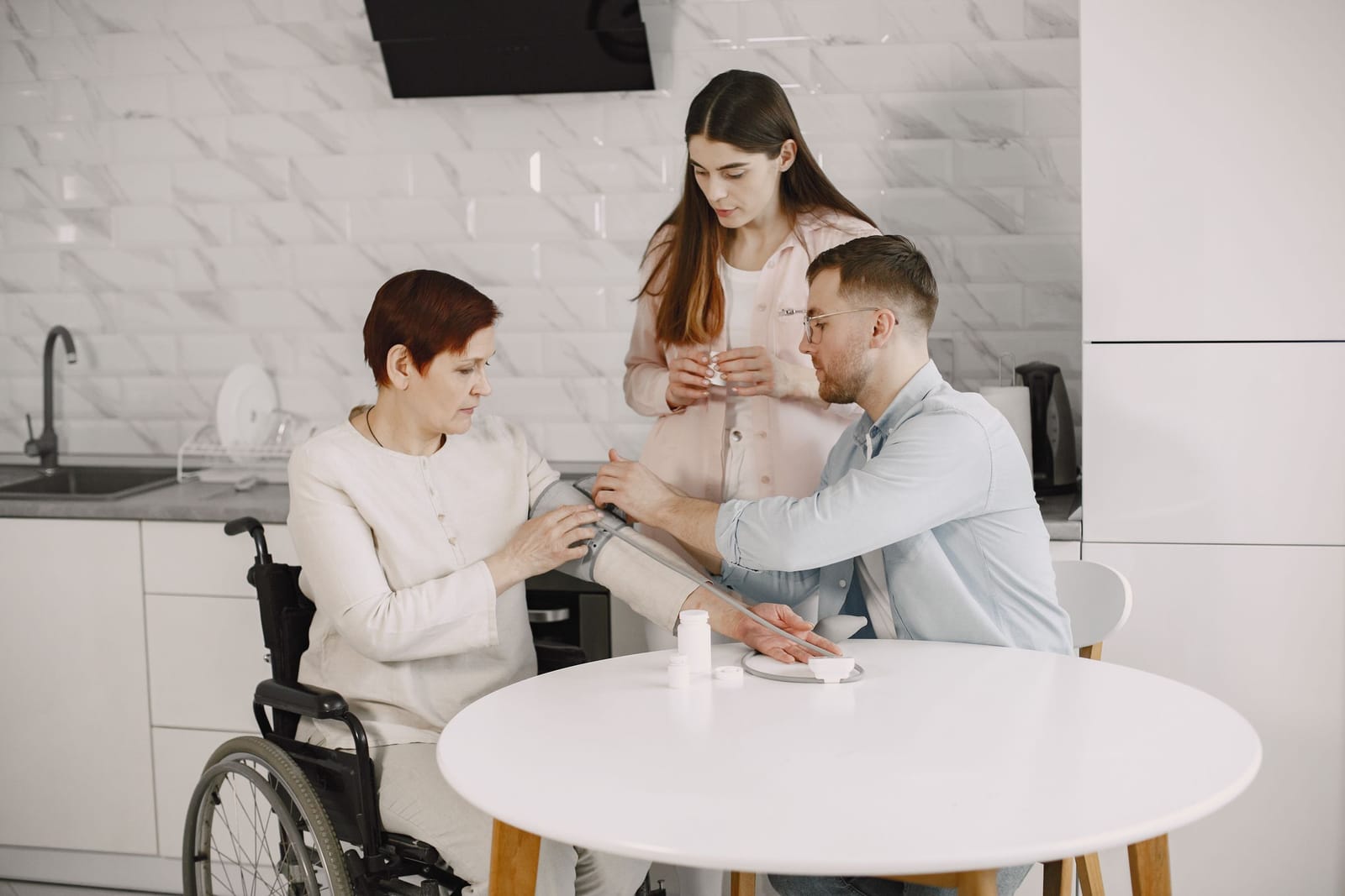 A young person in a wheelchair with family in the kitchen at home