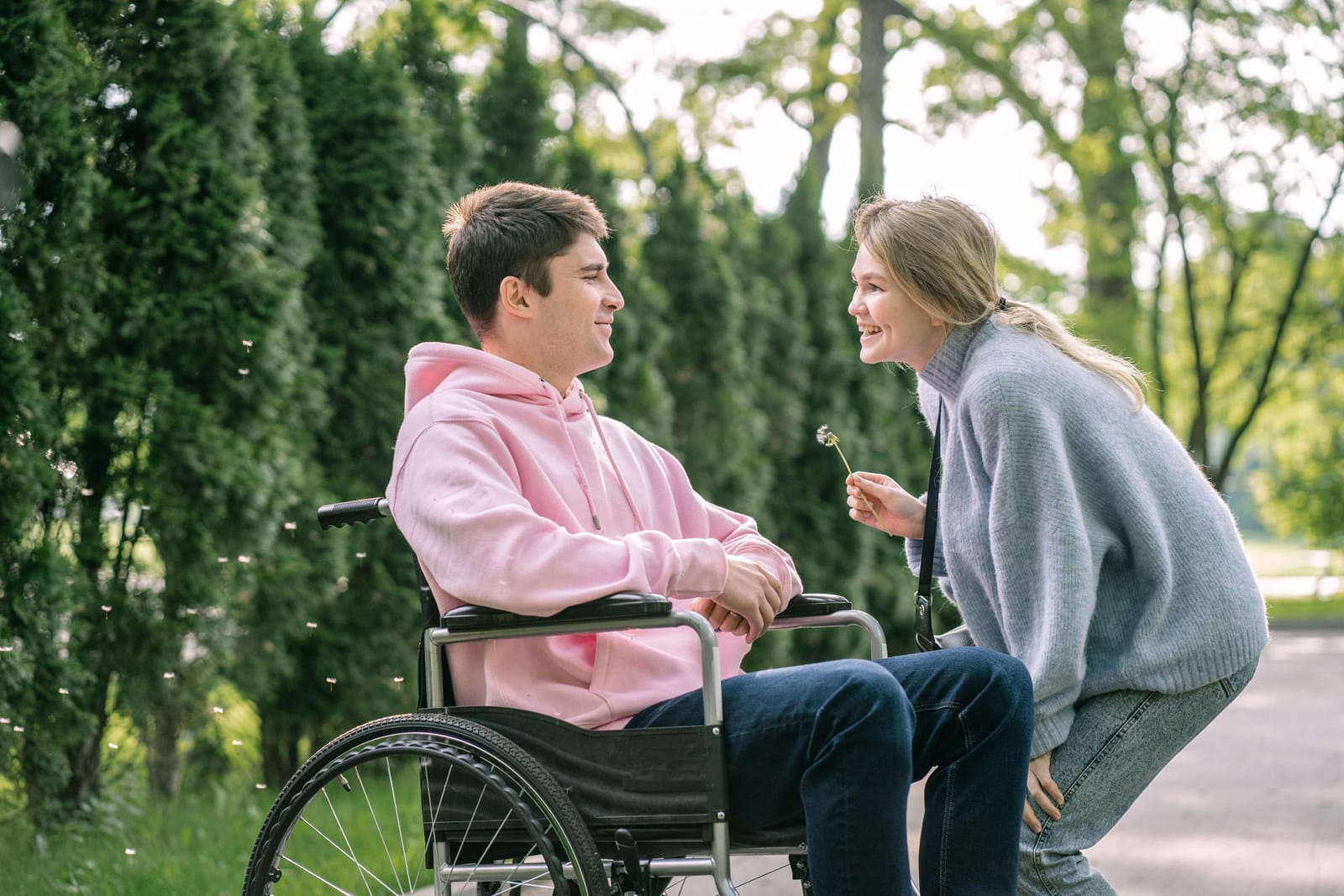 Two friends laughing together in a park, one seated in a wheelchair