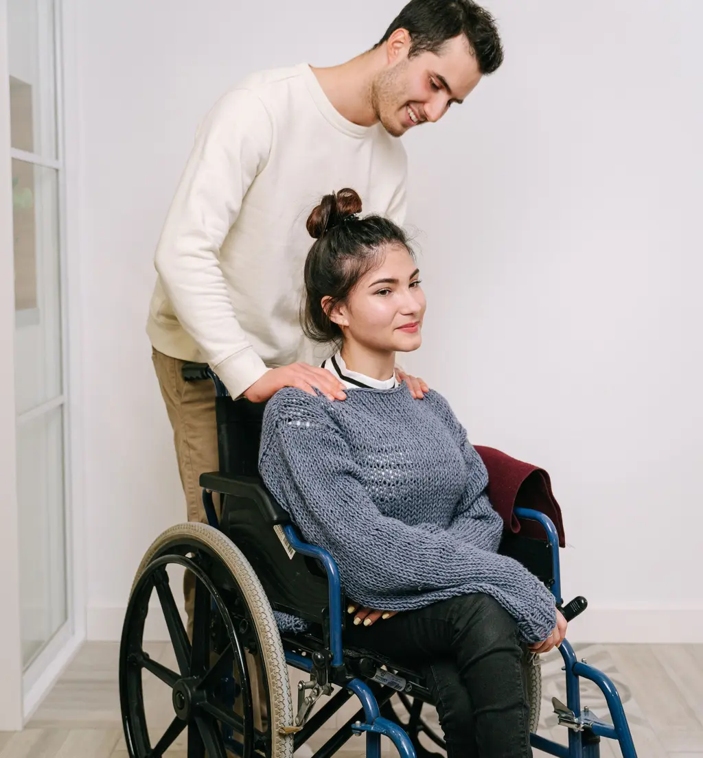 A support worker resting a reassuring hand on a young woman's shoulder in her wheelchair