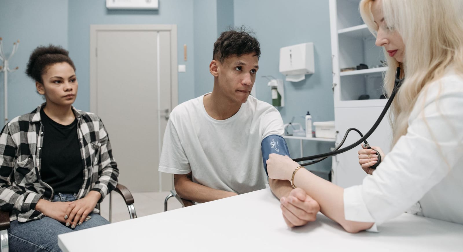 A nurse checking a young man's blood pressure while a friend sits with him