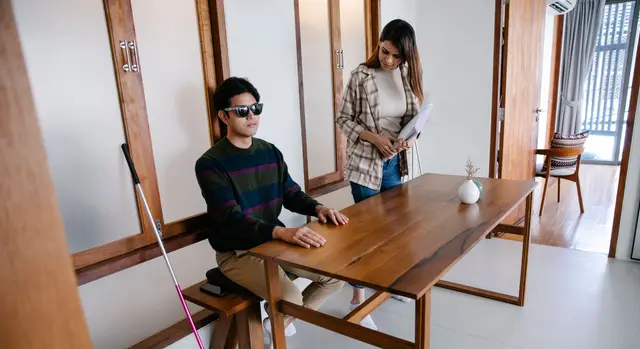 A support worker sitting with a man who is blind at his dining table at home