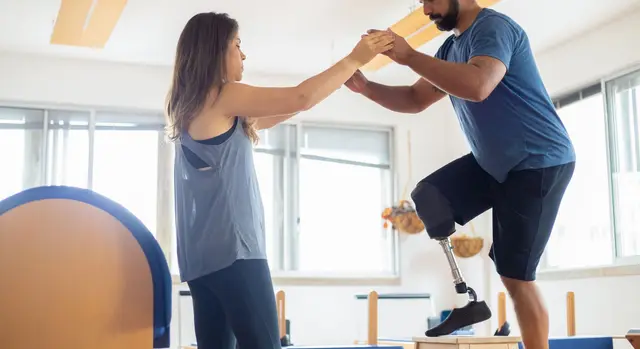 A support worker steadying a man with a prosthetic leg as he practises standing