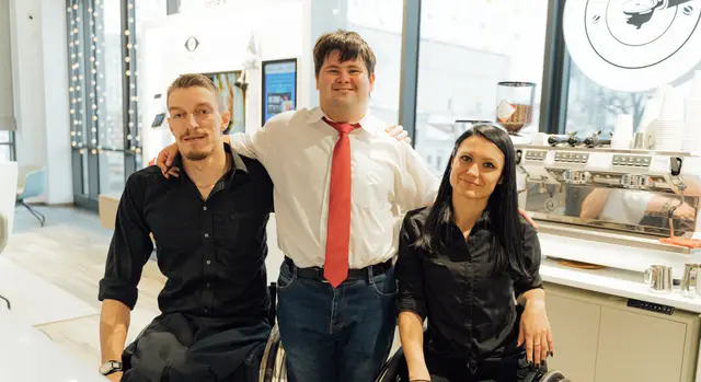 Friends laughing together around a cafe table, one of them a wheelchair user