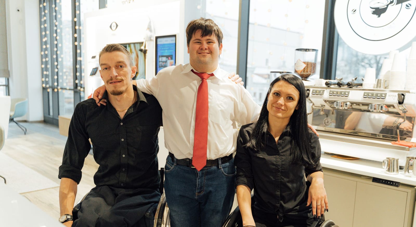 Friends laughing together around a cafe table, one of them a wheelchair user