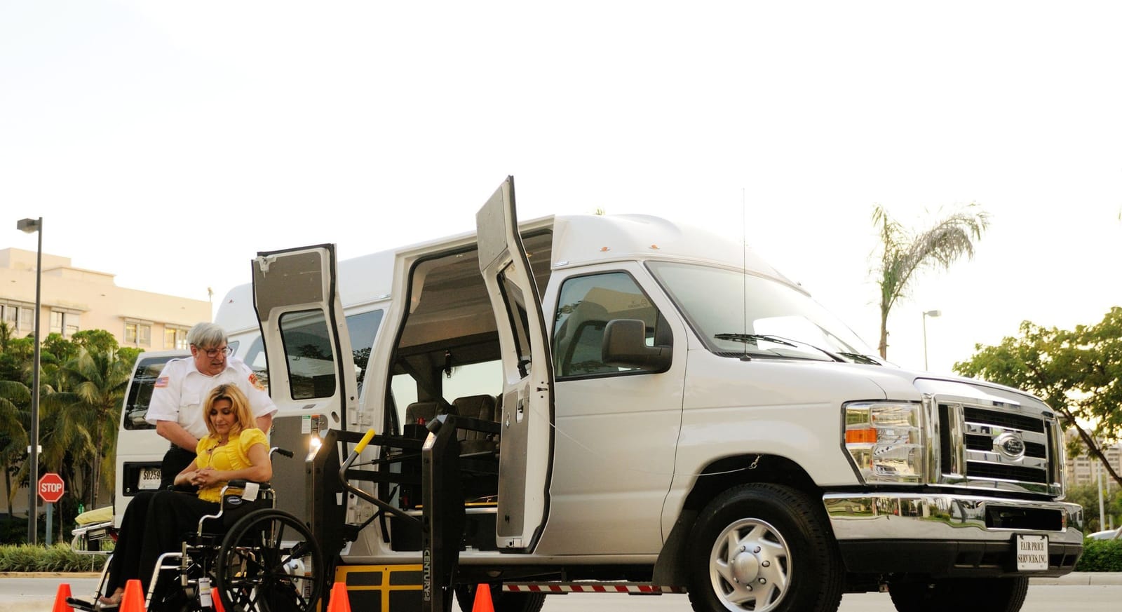 A wheelchair user boarding an accessible van by its ramp with the driver assisting
