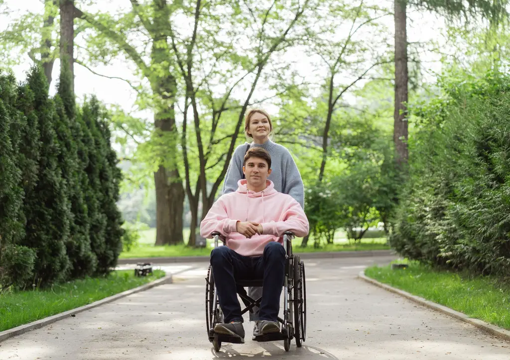 A support worker walking with a young man along a leafy park path
